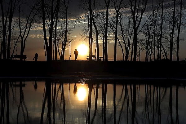 People stand and watch the sun set as they are reflected in a puddle at Presque Isle