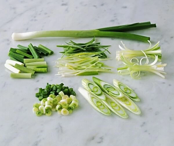 Whole, chopped and sliced spring onion on marble worktop