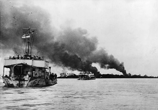 Landing craft travel up the Rangoon (Yangdon) river as smoke from an air strike