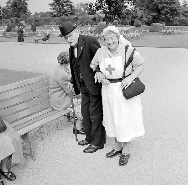 A Red Cross nurse helps and elderly gentleman to a bench during a day trip to Trentham