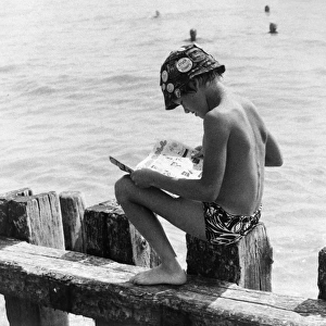 Boy sitting on breakwater reading a comic
