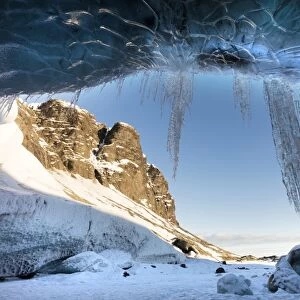 View from ice cave towards sunlit mountains with icicles hanging from cave entrance