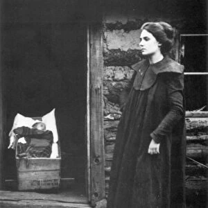 FRONTIER WOMAN & BABY. A woman on the Oregon frontier stands outside a cabin while her baby